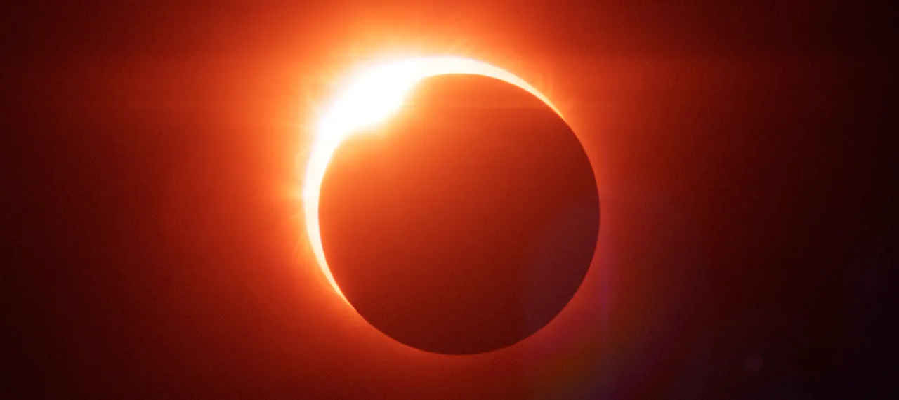 A solar eclipse: a black disk ringed by red and orange solar flares