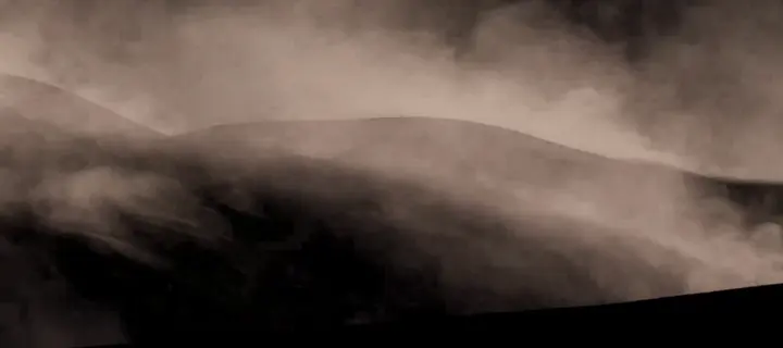 Billowing sand clouds rolling over a dune, on black
