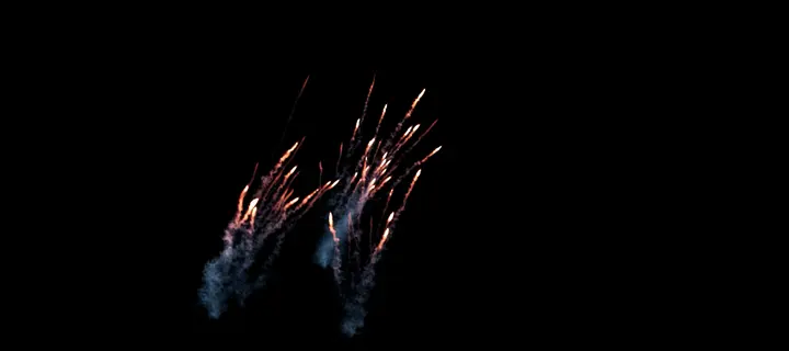 Sparks shooting out of the blast, trailing blue smoke, on black