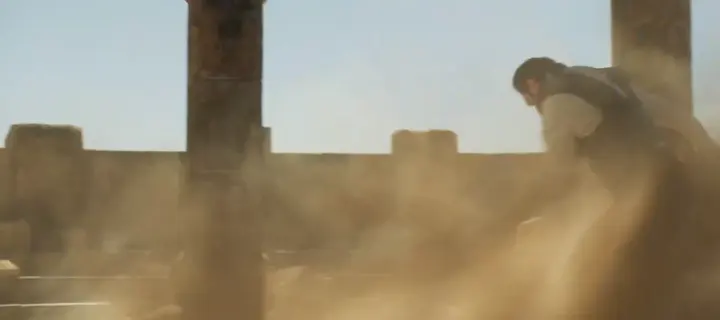 A man thrown back by a blast of dust among ruined stone pillars